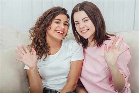 Two Amazing Girls Sitting On The Sofa Hugging One Another Smiling At
