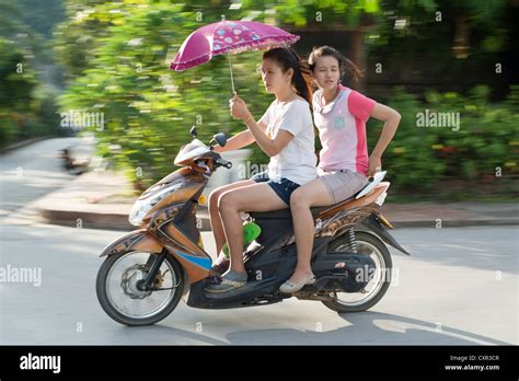 Two young women speed past on a motor scooter in Luang Prabang, Laos ...
