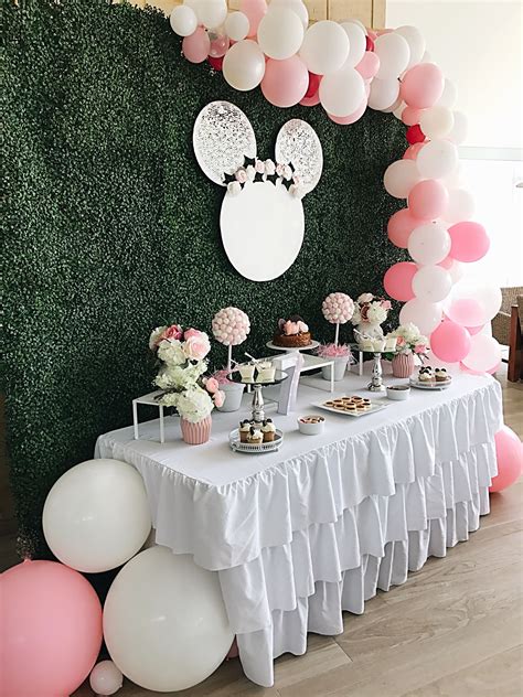 A Table Topped With Lots Of Desserts And Balloons Next To A Wall Covered In Greenery