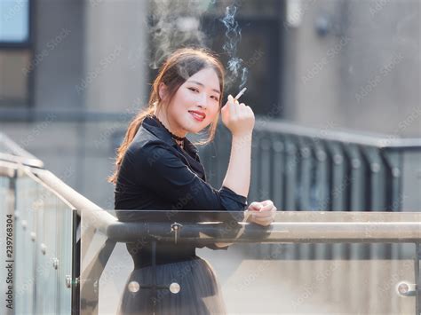 portrait of beautiful chinese girl in black dress smoking a cigarette outdoor in sunny day