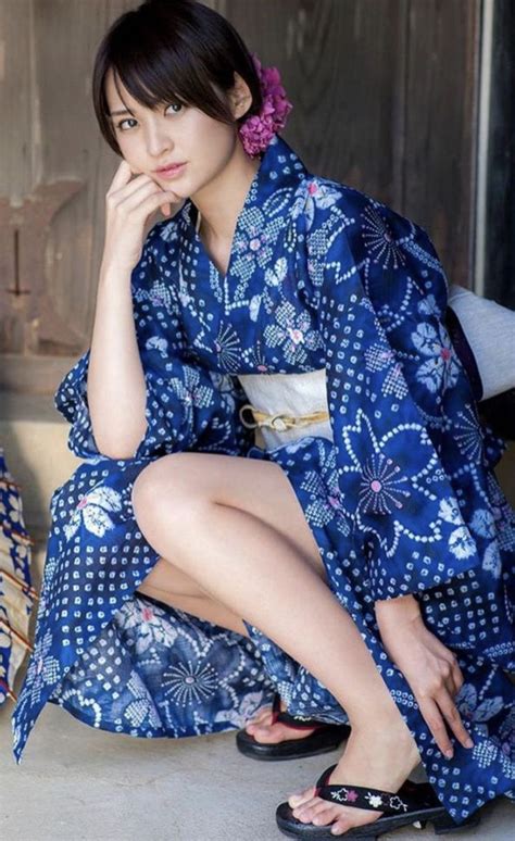 a woman in a blue kimono sitting on the ground with her hand under her chin