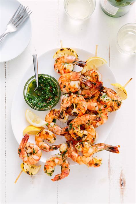 Two skewers of shrimp on a white platter with lemon slices and parsley. Recipe: Grilled Shrimp Skewers with Chimichurri | Kitchn