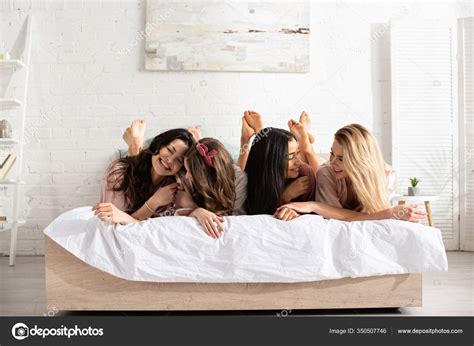 mujeres multiétnicas sonriendo mirándose descansando cama despedida soltera fotografía de stock