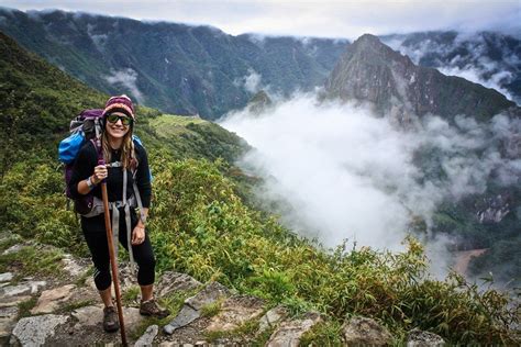 A Woman Hiking Up The Side Of A Mountain With Fog In The Valley Behind Her