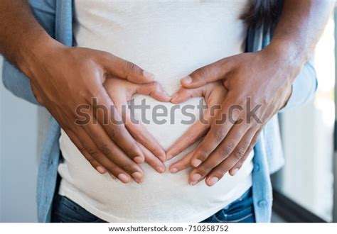 「妊娠中の妻の腹を抱く黒人。妊娠中の女性と愛する夫が家でおなかを抱きしめる。妊婦の腹の多民族カップルの手の中。」の写真素材（今すぐ編集