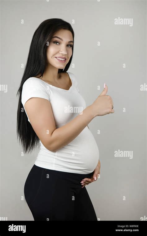 Beautiful Pregnant Brunette Woman Holding Her Pregnant Belly With One Hand And Showing Like Sign