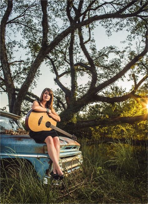 A Woman Sitting On Top Of An Old Car Holding A Guitar