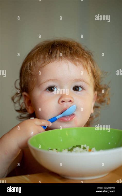 Funny Baby Eating Food Himself With A Spoon On Kitchen Child Nutrition