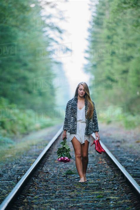 Teenage Girl Walking Along Train Track Holding Red Shoes And Flowers