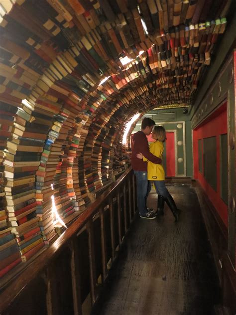A Man And Woman Standing In Front Of A Tunnel Filled With Books