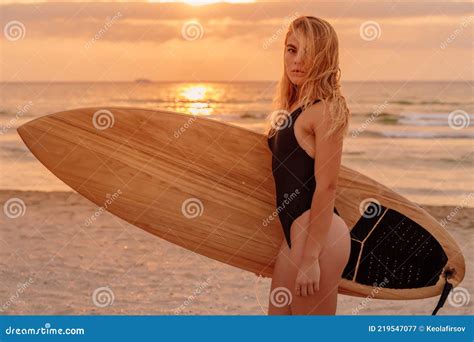 portrait of blonde surfer woman on beach at warm sunset or sunrise surf girl with surfboard