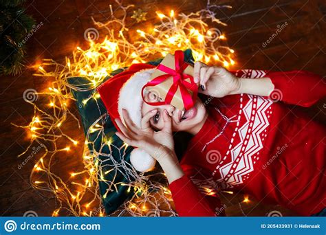 Funny Cute Woman Lying On Floor And Holding Present In Room With Christmas Decorations At Home