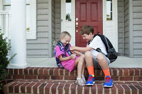 Older Brother Tickles Little Sister While Sitting On Brick Front Porch