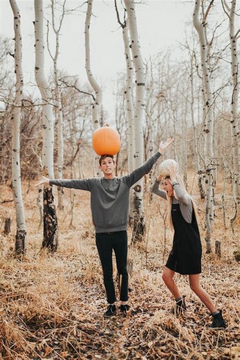 A Man And Woman Standing In The Woods With An Orange Pumpkin On Their Head