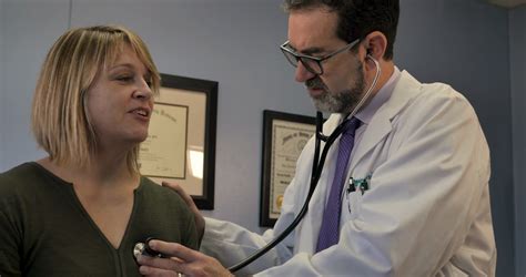 Male Doctor Using A Stethoscope On A Female Patient To Listen To Her