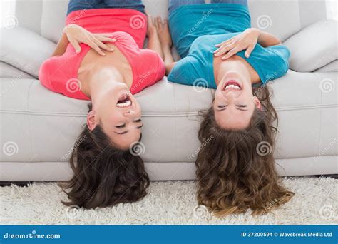 Cheerful Friends Lying Upside Down On Sofa At Home Stock Photo Image