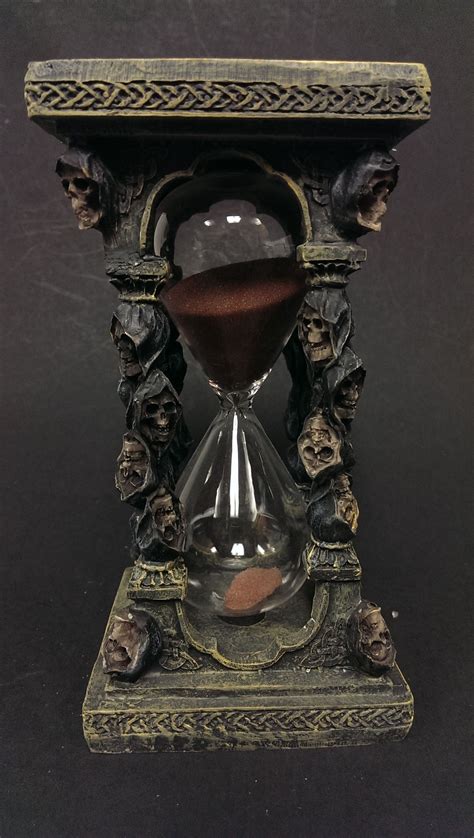 An Old Fashioned Hourglass Is Sitting On A Black Surface With Skulls