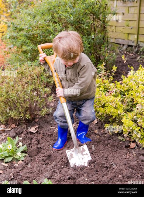 Two Year Old Boy Digging In The Garden Playing With Soil Stock Photo