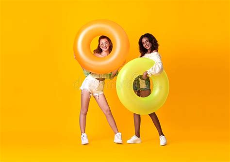 Cheerful Friends Woman Dressed In Summer Clothes Holding Rubber Ring Over Yellow Background