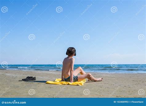 Teen Boy Is Sitting On Yellow Towel In The Headphones And Sunbathes On