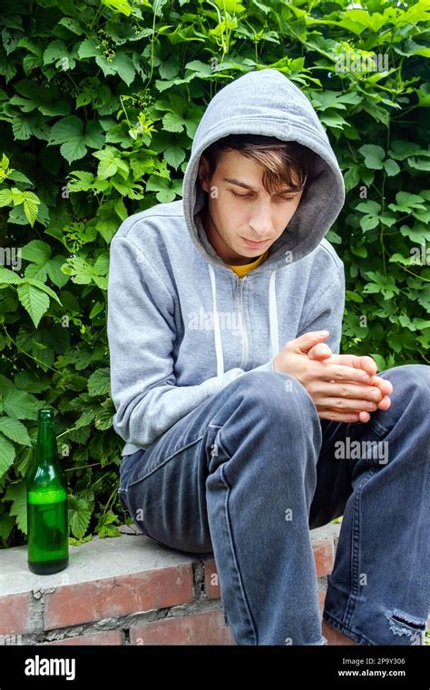 Sad Young Man In A Hoodie With A Beer Bottle On The Sidewalk Of The