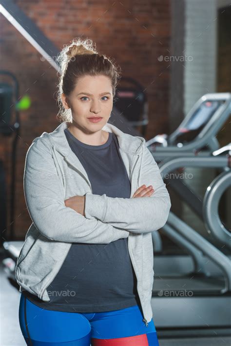 Overweight Woman Standing At Gym With Arms Crossed And Looking At