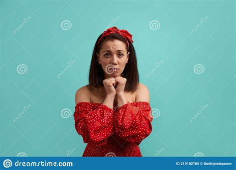 upset woman in red dress holds hands clenched in fists near face looking somewhere waiting for