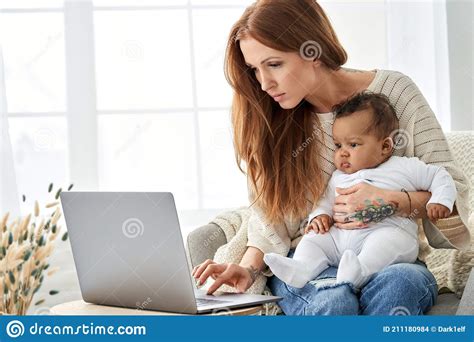 Busy Mother Using Laptop Working From Home With Little African Baby