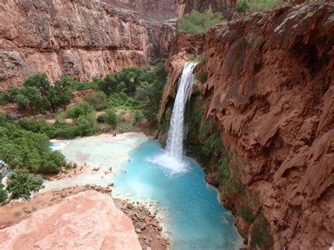 A Waterfall In The Middle Of A Canyon With Blue Water Running Down Its
