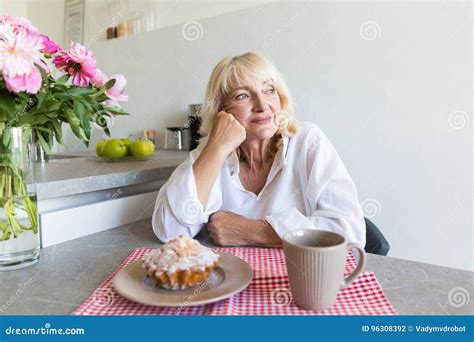 Thoughtful Senior Woman Sitting At The Kitchen Table Stock Photo