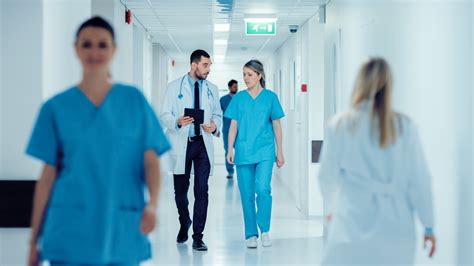 Surgeon And Female Doctor Walk Through Hospital Hallway They Consult