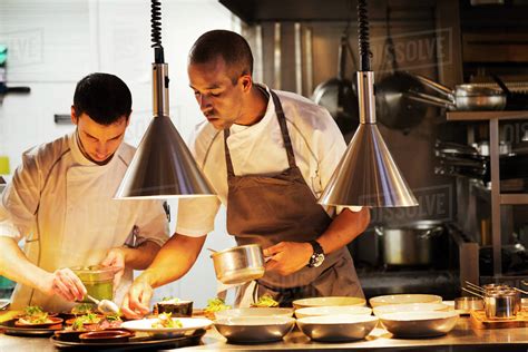 Two Chefs Standing In A Restaurant Kitchen Plating Food