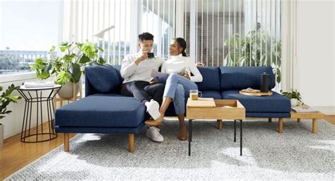 A Man And Woman Sitting On A Blue Couch Looking At Their Cell Phones In The Living Room