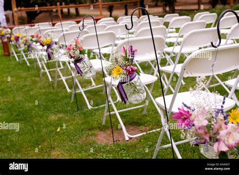Ceremony Seating With White Chairs And Flowers At An Outdoor Wedding