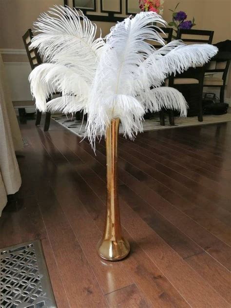 There Is A Vase With White Feathers In It On The Floor Next To A Dining