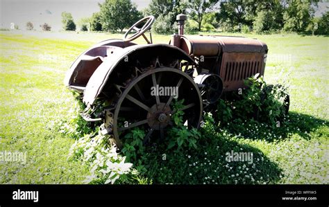 Old Tractor On Grassy Field Against Trees Stock Photo Alamy