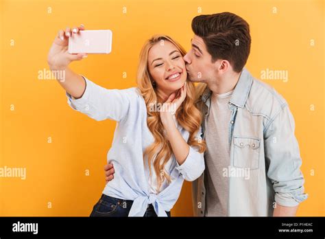 Portrait Of Lovely Couple Taking Selfie Photo On Mobile Phone While Man Kissing Woman On Cheek