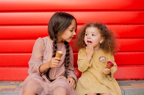 Premium Photo Two Girls Eat Ice Cream Near The Red Fence One