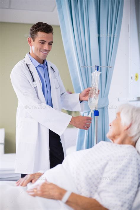 Doctor Adjusting Iv Drip While Patient Lying On Bed Stock Photo By