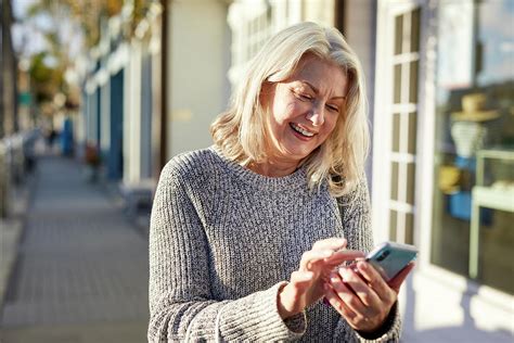 Smiling Senior Woman Using Smart Phone While Standing On Sidewalk In