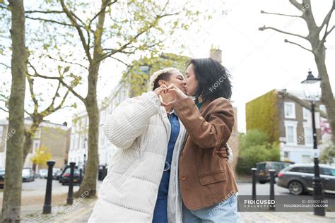 Affectionate Lesbian Couple Kissing While Gesturing Heart Shape — Outdoors Multiethnic Stock