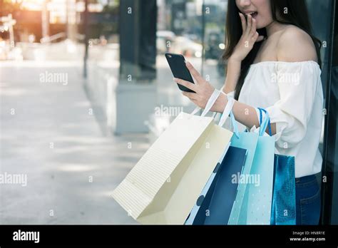 Young Aisin Woman Using Her Smartphone And Hold Shopping Bag While