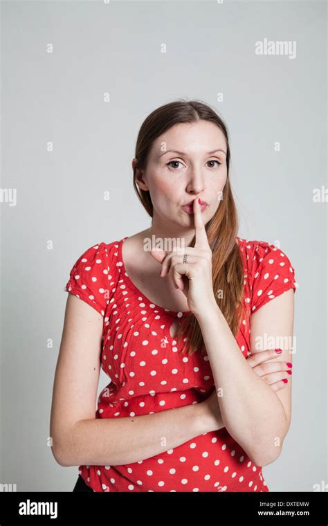 Studio Portrait Of Attractive Woman With Finger Over Pursed Lips To