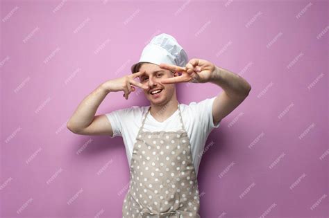Premium Photo Young Guy Housewife In Apron And Hat Poses And Shows Peace Sign With His Fingers