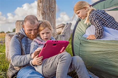 Handsome Redhead Father And Blonde Daughters Using A Tablet Whilst Enjoying A Camping Holiday