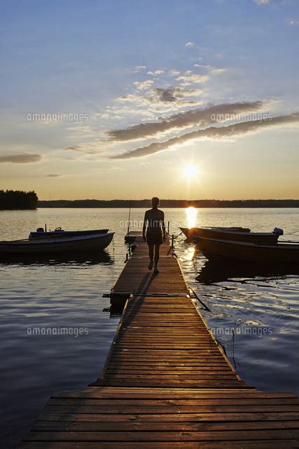 Sweden Vastra Gotaland Skagern Woman walking on pier in lake at sunset の写真素材イラスト