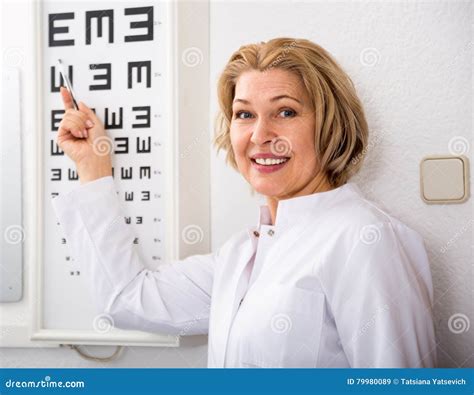Smiling Female Ophthalmologist Pointing At Letters Of Eye Chart Stock