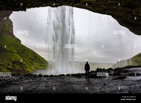Female Hiker Looking At Seljalandsfoss Waterfall Inside A Cave Stock