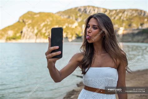 Young Woman Sticking Out Tongue While Taking Selfie Through Smart Phone