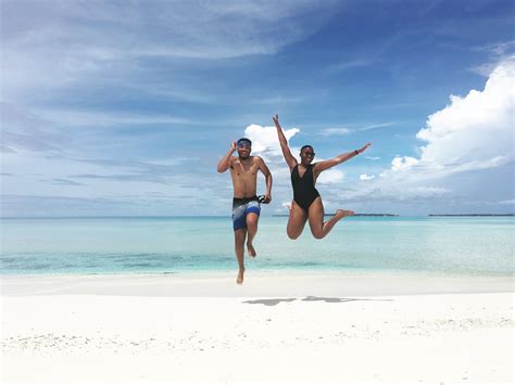 Two People Jumping In The Air On A Beach With Clear Blue Water And White Sand